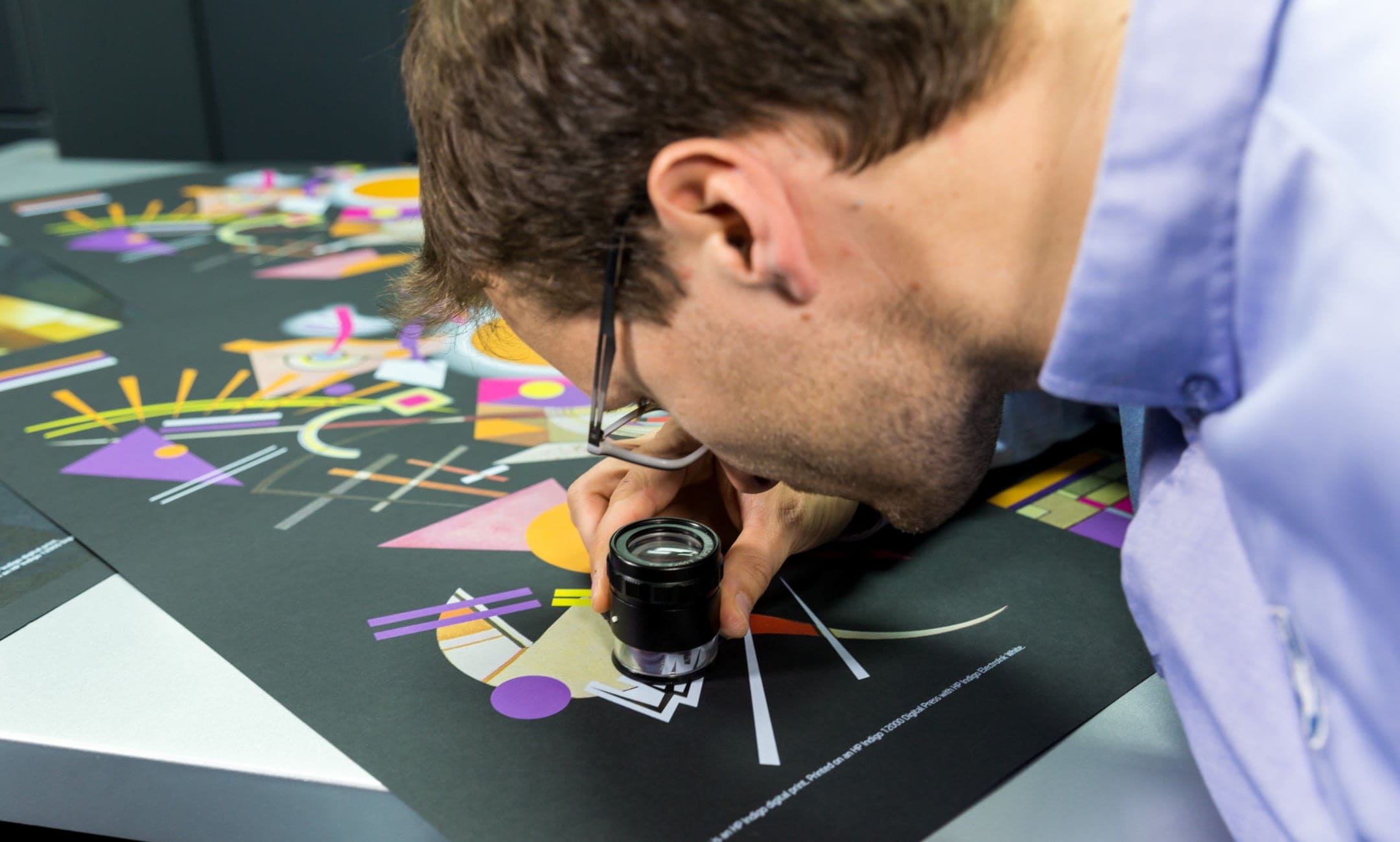 Expert checking the quality of HP Indigo print with a loupe