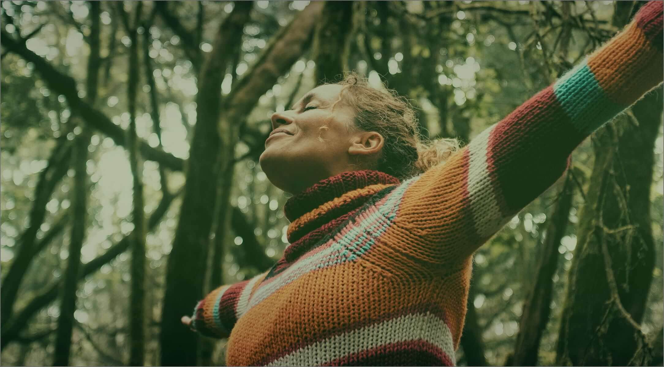 Mulher com os braços esticados, cercada por árvores