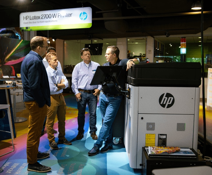 Five men are engaged in a conversation in a printing room. The room is equipped with an HP press.