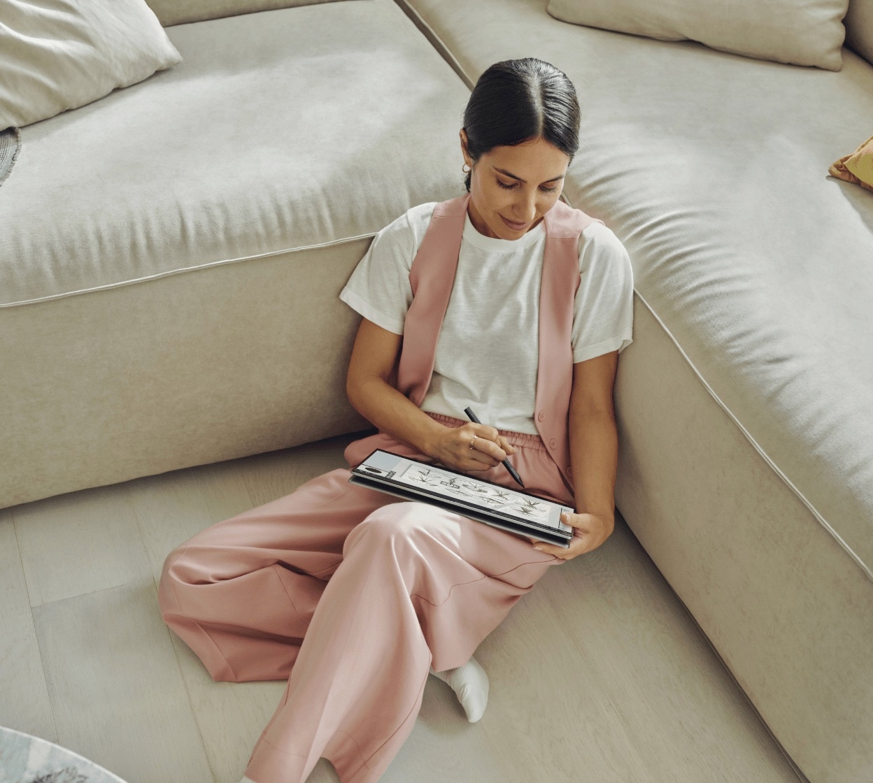 A woman designing on an HP laptop in tablet mode using an HP pen while sitting on the floor aside her couch.