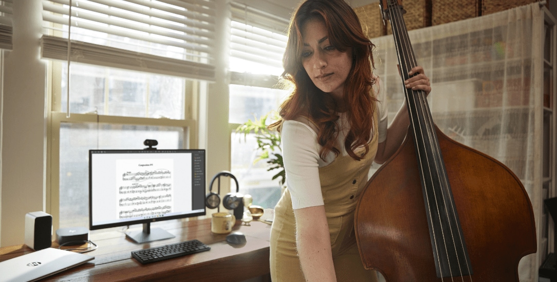 Woman practicing cello, with HP monitor and accessories in the background