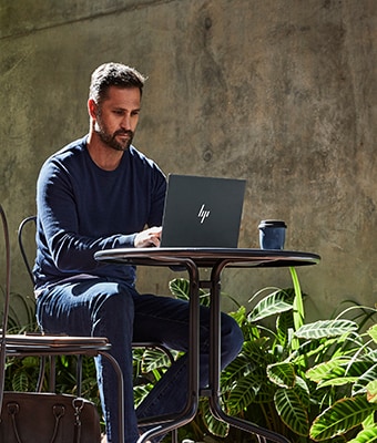 Homme assis à une table en extérieur, en train de travailler sur un ordinateur portable