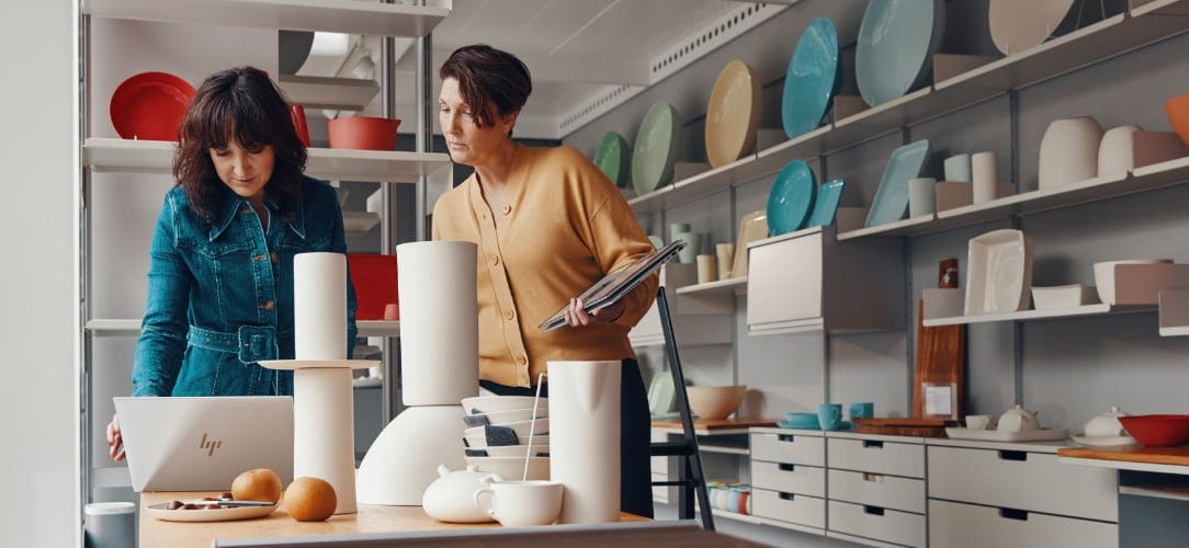 Two women using HP EliteBook laptop in ceramics display shop