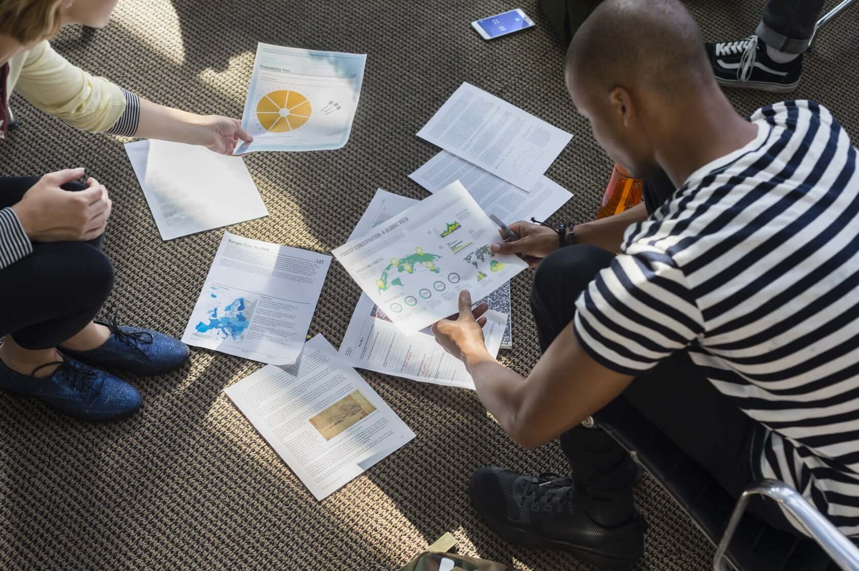 Young male teacher with students looking at color prints arranged on classroom floor