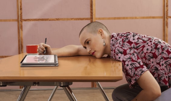 A woman reclined over a table drawing on an HP Chromebook in tablet mode