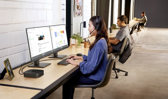 A woman having a virtual conference on her HP Chromebox connected in two HP monitors, aside of her 2 co-workers.