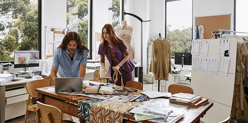 A man showing some close designs to his co-worker on his HP laptop.