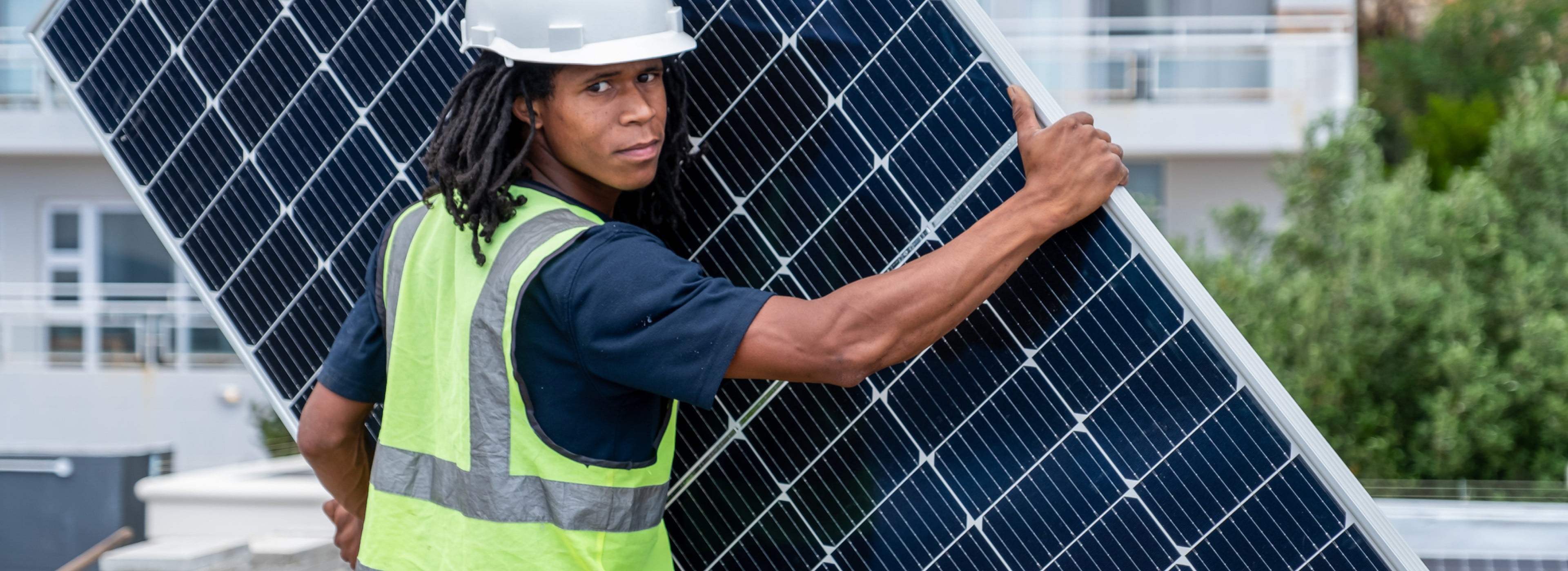 Un ouvrier porte un grand panneau solaire pour l’installer.