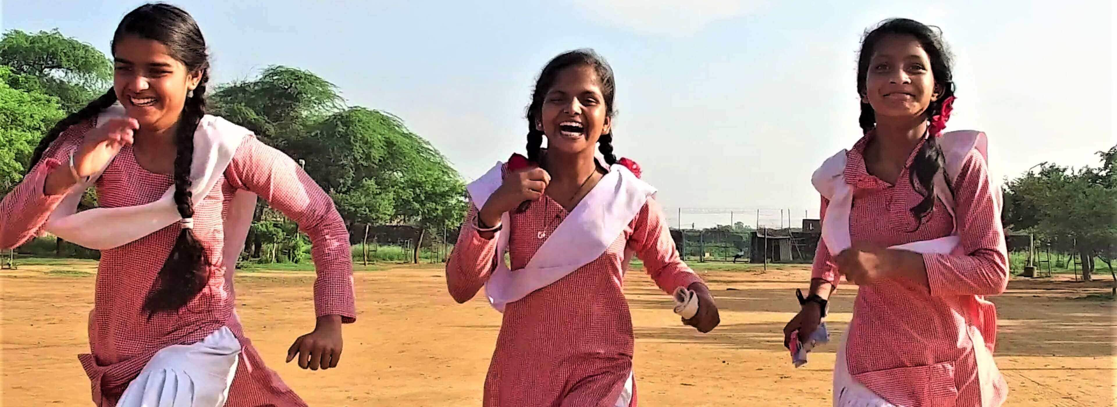 Three girls wearing pink dresses running while laughing.