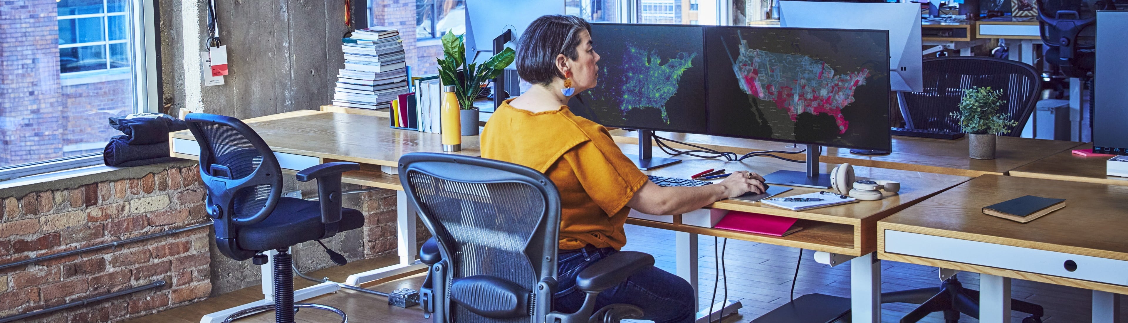 Frau an großem Arbeitsplatz in einem Büro, die eine Analyse durchführt, mit zwei großen Monitoren,  Maus und Tastatur mit einer Workstation