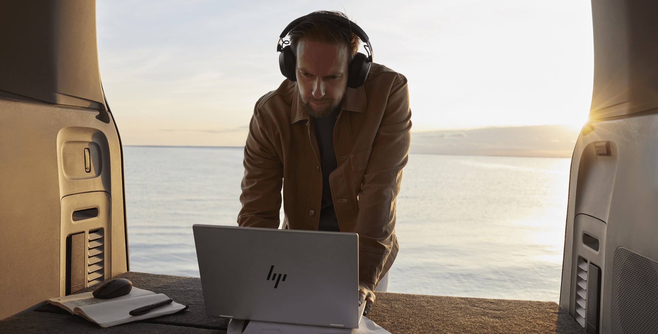 Man working on an HP laptop on top of his van in front of a lake