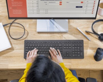 Top view of a woman working in front of an HP Monitor connected to a closed HP Laptop