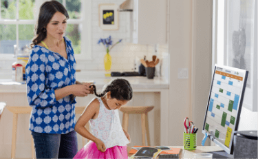 Mother viewing a schedule on an HP Monitor while combing her daughter's hair