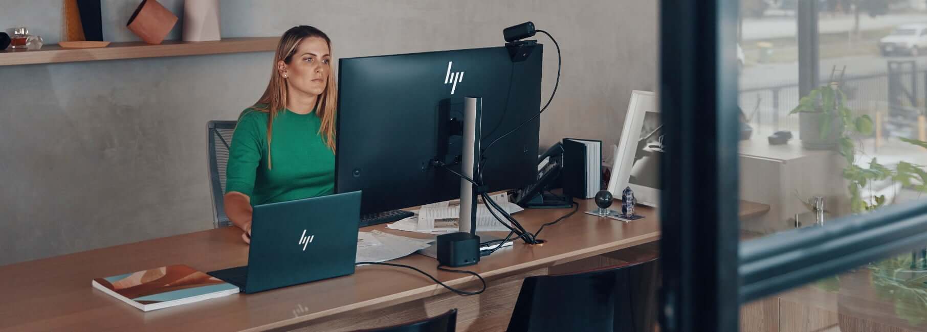 A woman working in front of an HP monitor connected to an HP laptop via an HP docking station