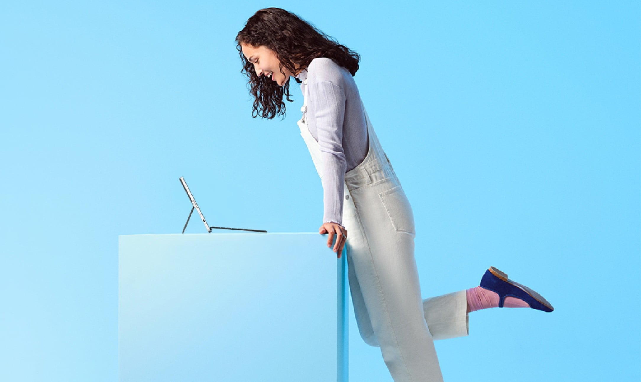 A young woman having fun with her HP convertible laptop while standing on a blue background.