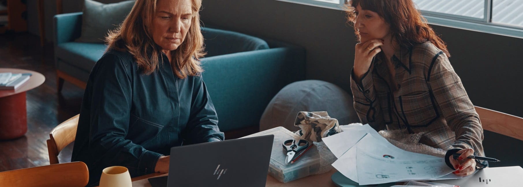 Two women working on some cloth designs while using an HP laptop.