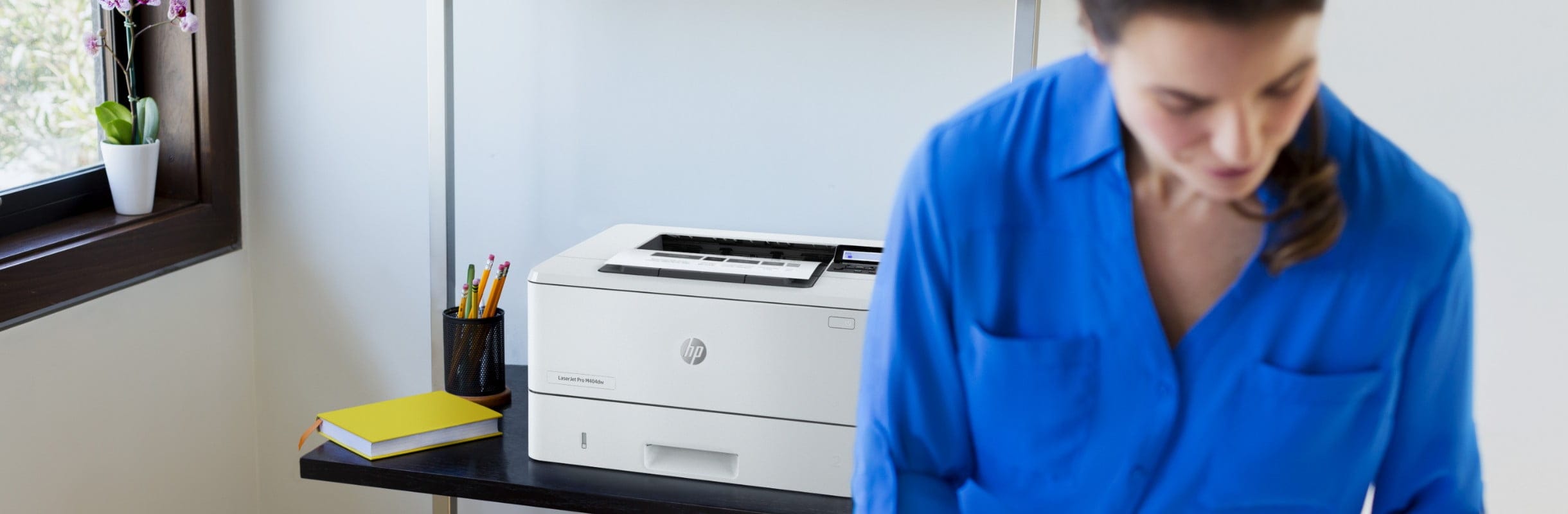 A woman checking some prints while standing aside an HP LaserJet Pro M404