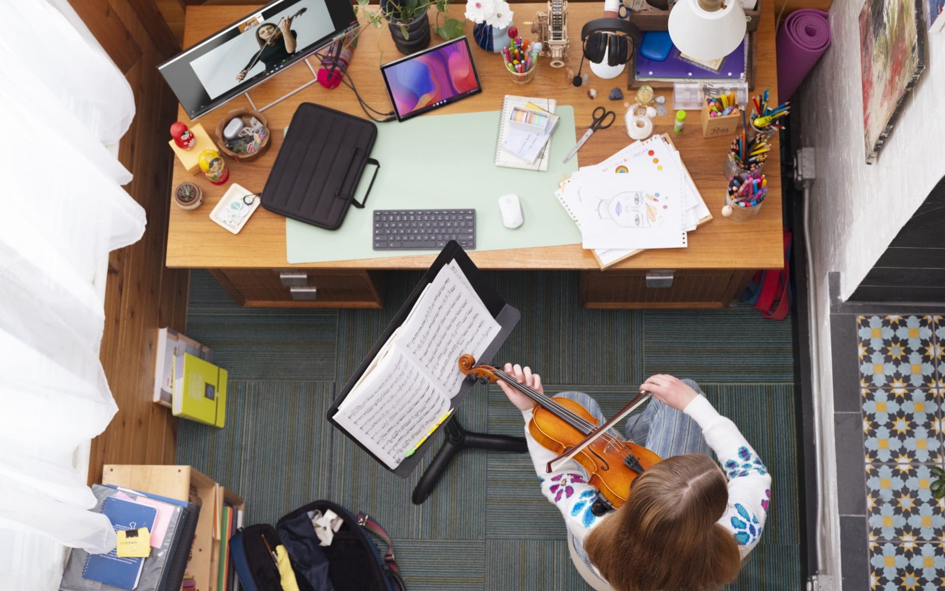 A woman playing a violin on front of her desk seen on top view with an HP tablet with a wireless keyboard and mouse.