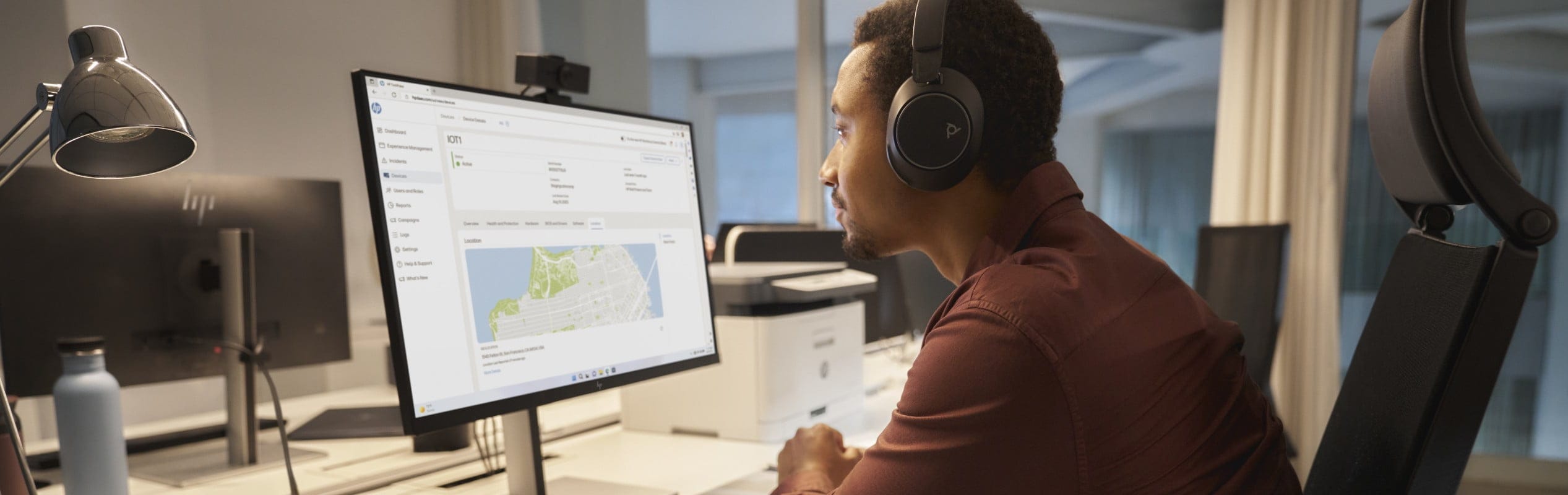 A man looking at a map on an HP monitor with an HP webcam while using a Poly headset.