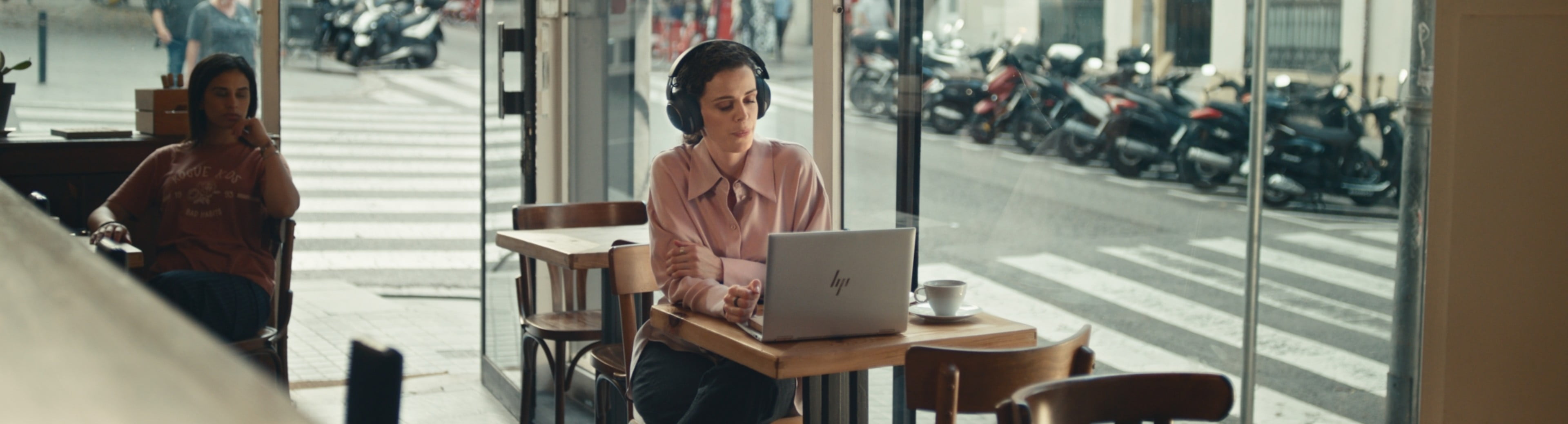 Een vrouw met een bril en blauwe trui die een Spectre x360-laptop vasthoudt in een kantoor met kleurrijke schilderijen aan de muur.