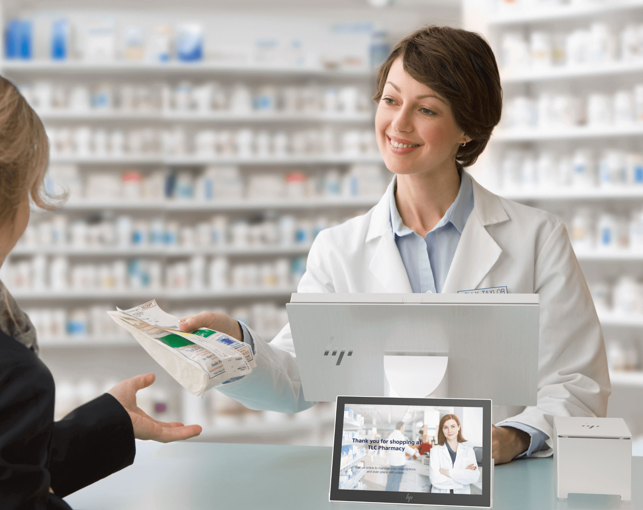 Female pharmacist handing out medication to a customer, an HP Engage point of sale system and an HP receipt printer are at the checkout counter