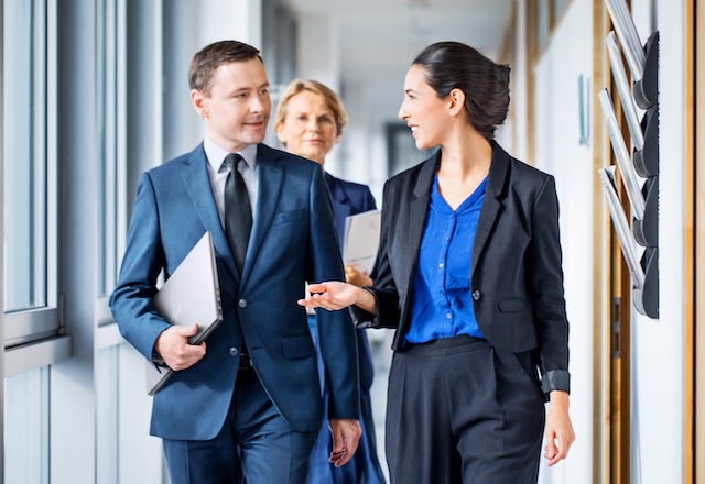 Man carrying an HP laptop while walking on a hallway with his two female co-workers