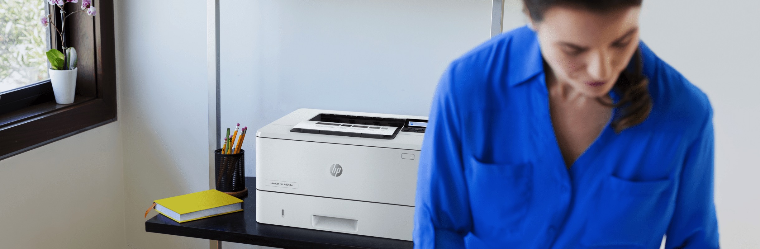 A woman checking some prints while standing aside an HP LaserJet Pro M404