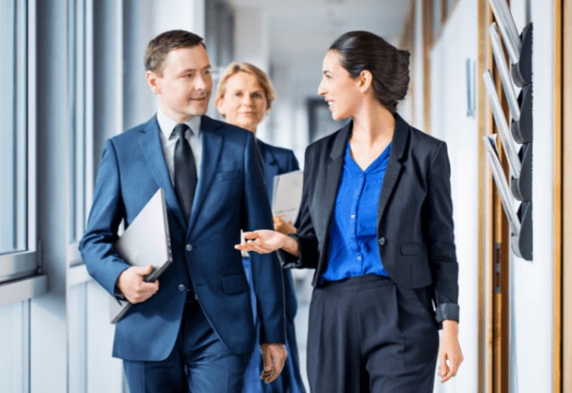 Man carrying an HP laptop while walking on a hallway with his two female co-workers