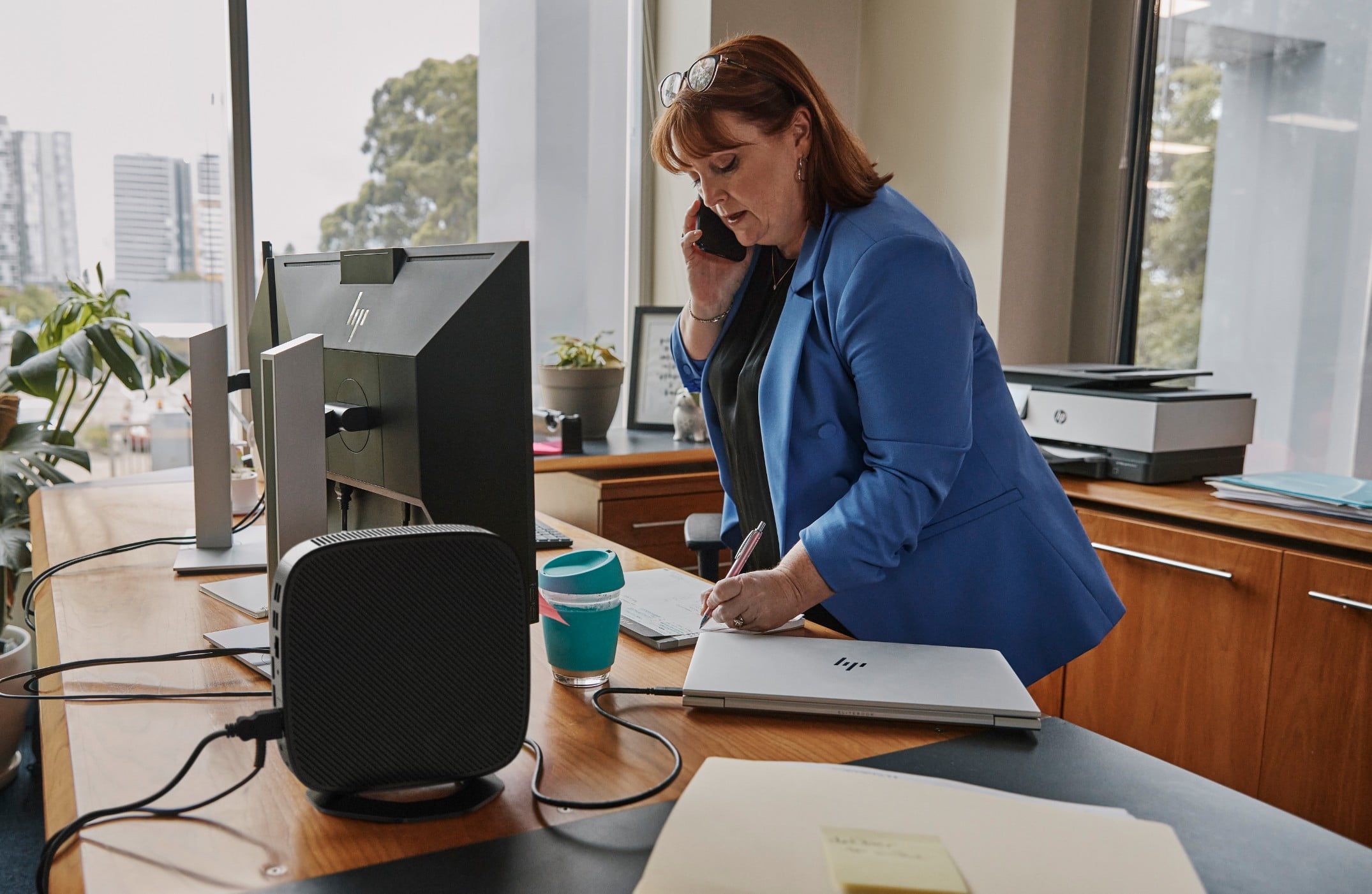 A woman taking some notes aside an HP laptop and an HP desktop connected to an HP monitor.