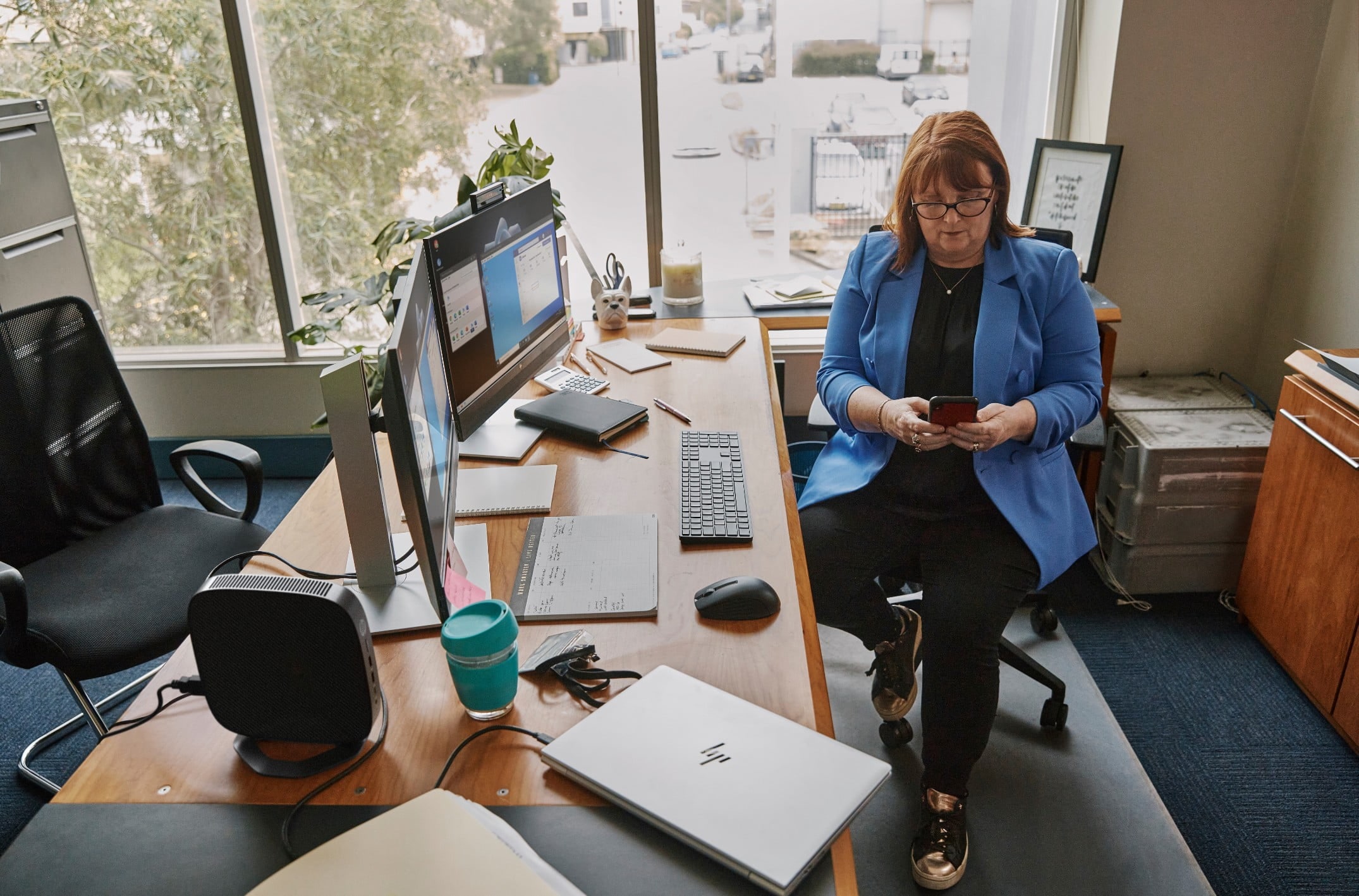 A woman sitting aside her HP dual monitors connected to an HP laptop with a wireless keyboard and mouse.