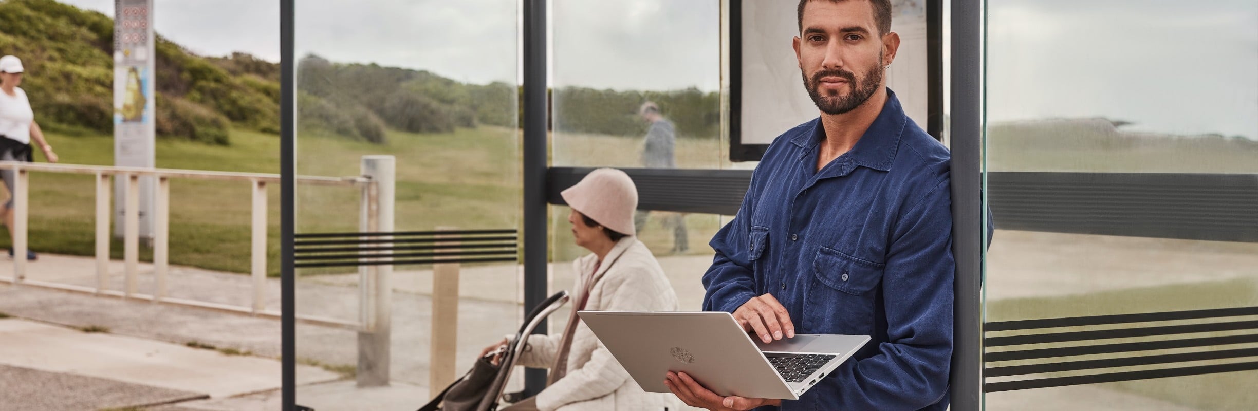 A man using a laptop while standing at a bus stop.