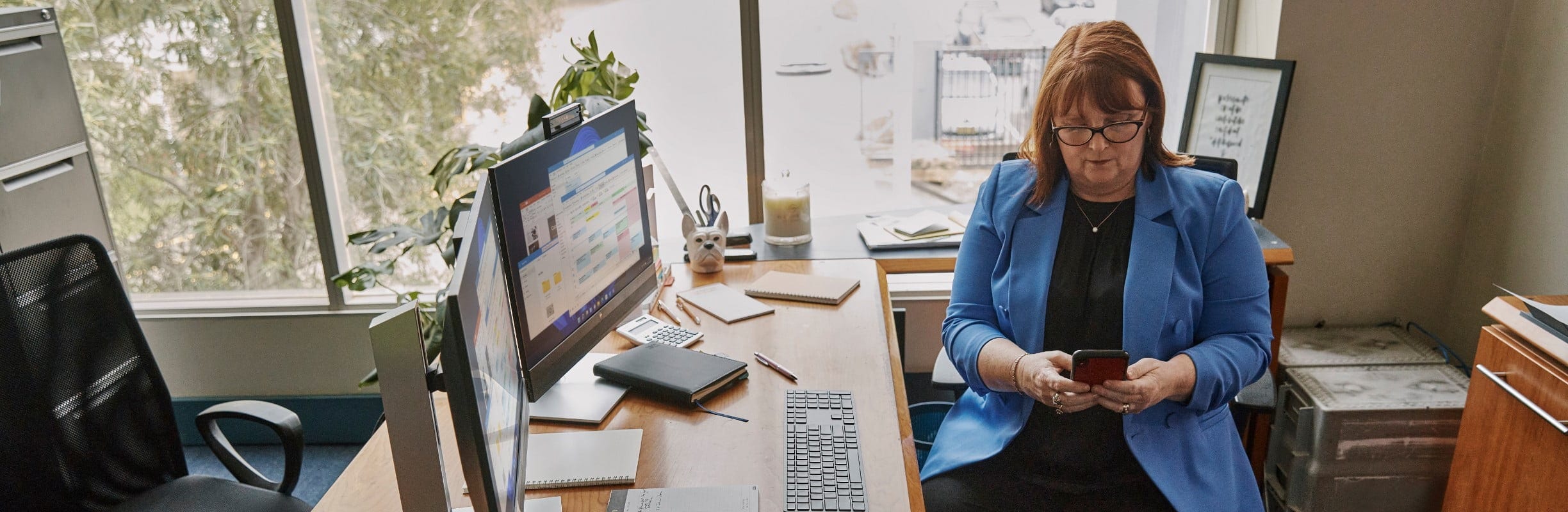 A woman using her cell phone while sitting at her desk.