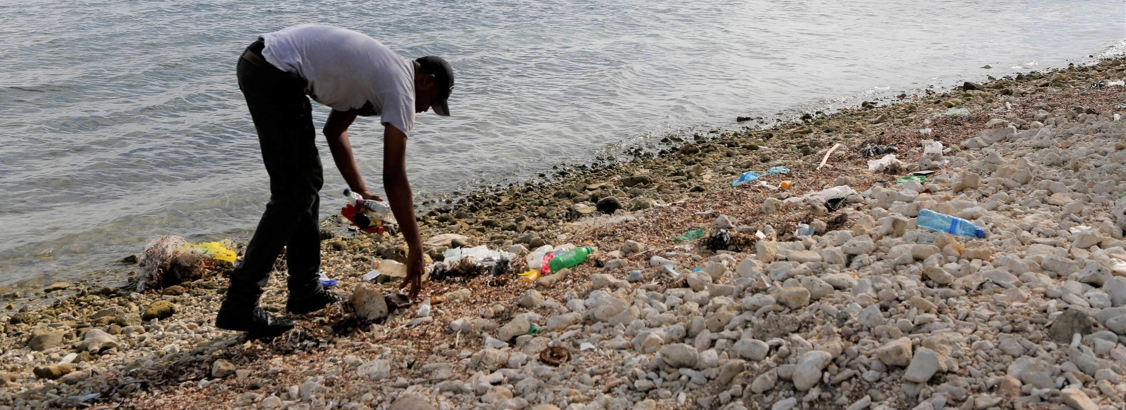 Ein Mann reinigt den Sandstrand am Meer von zu recycelnden Plastikflaschen.