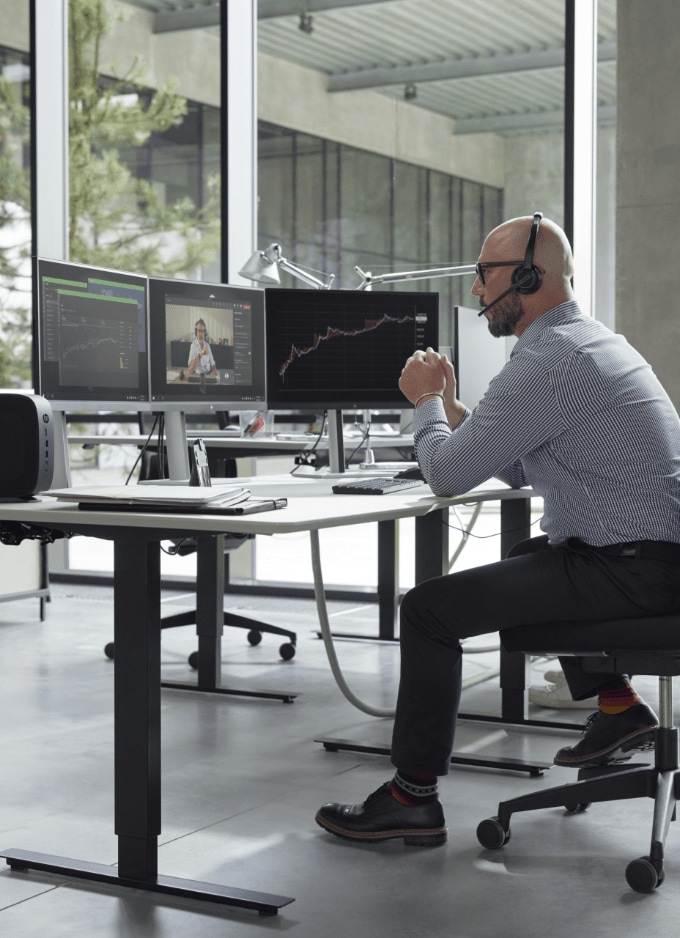 Ein Mann prüft bei einer virtuellen Konferenz Daten an drei miteinander verbundenen HP Monitoren.