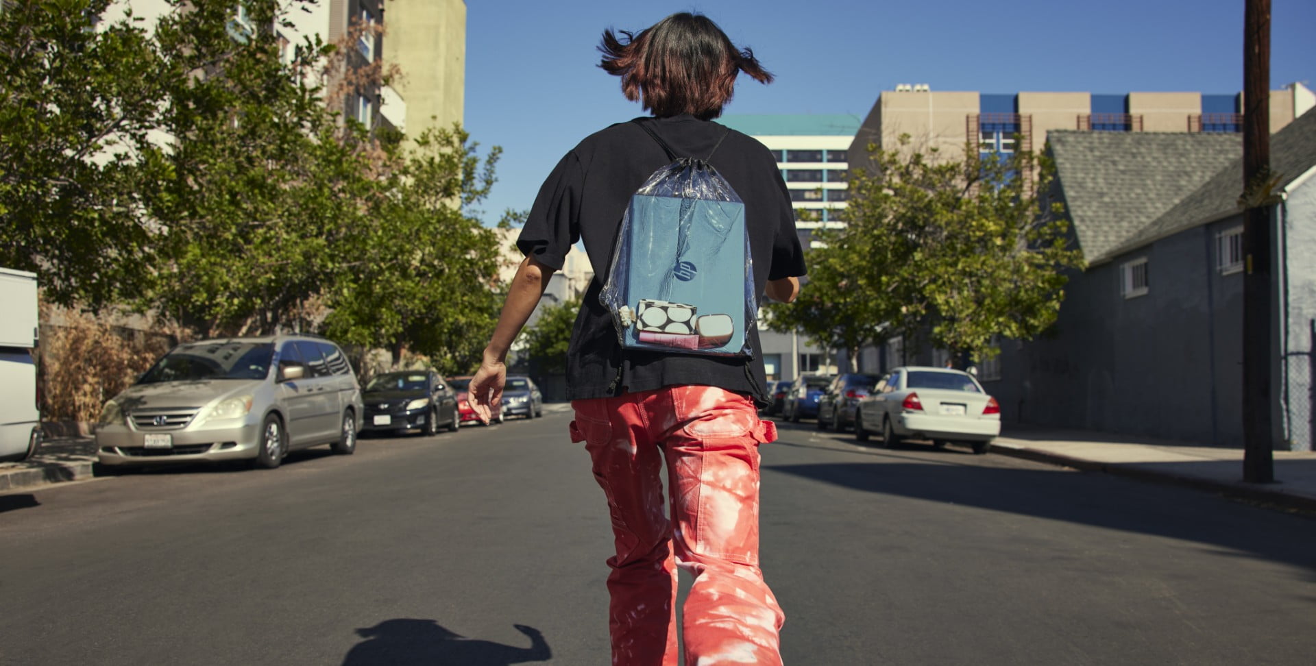 A kid skating to the school with an HP laptop inside his transparent bag on his back.