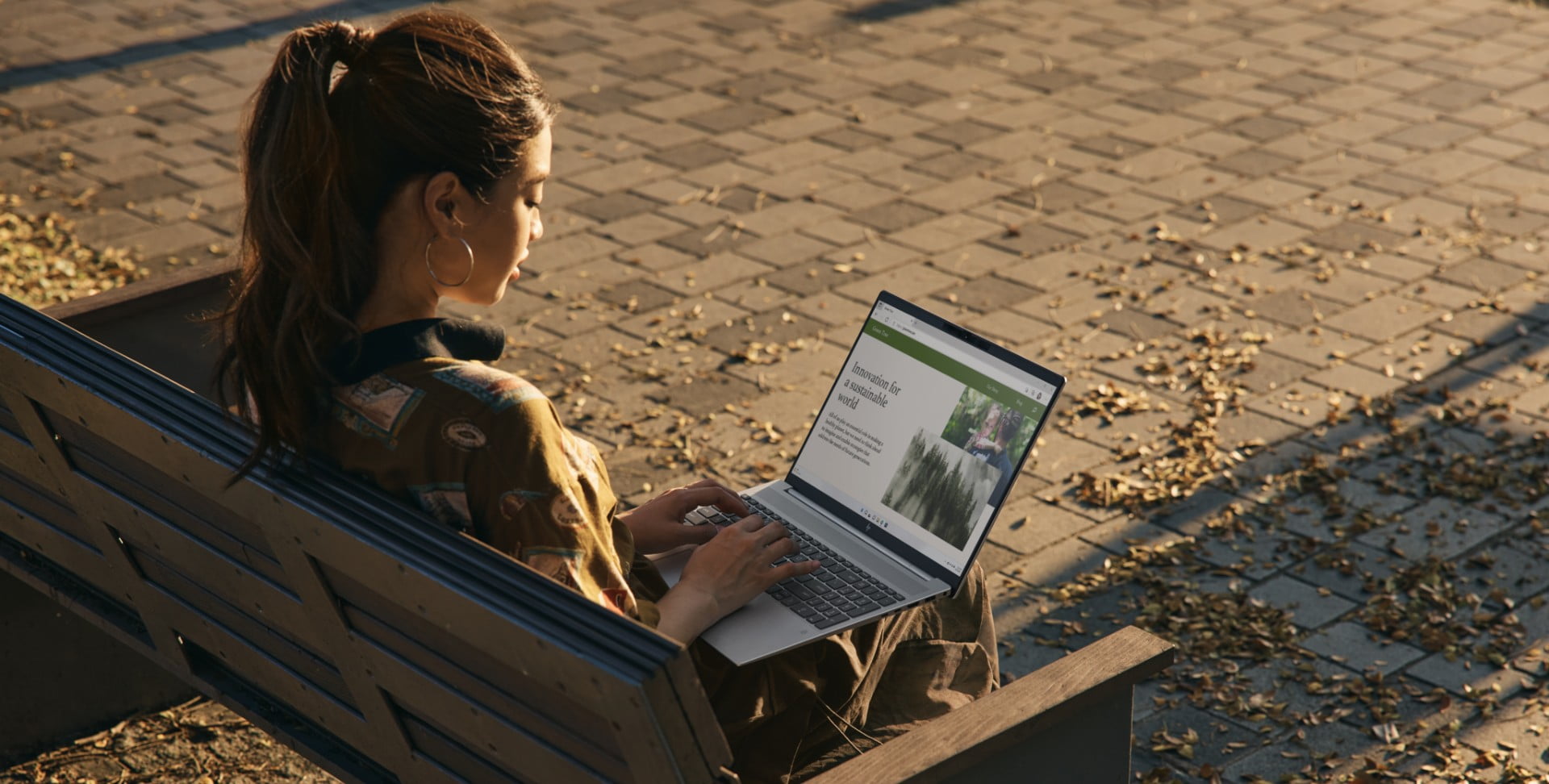 A person sitting outside on a bench using a Pavilion laptops