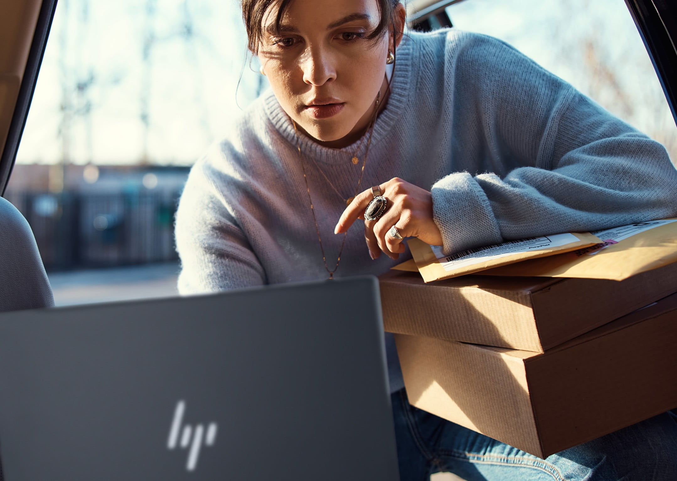 Eine Frau nutzt einen HP Spectre x360 Laptop, während sie einige Kartons trägt.