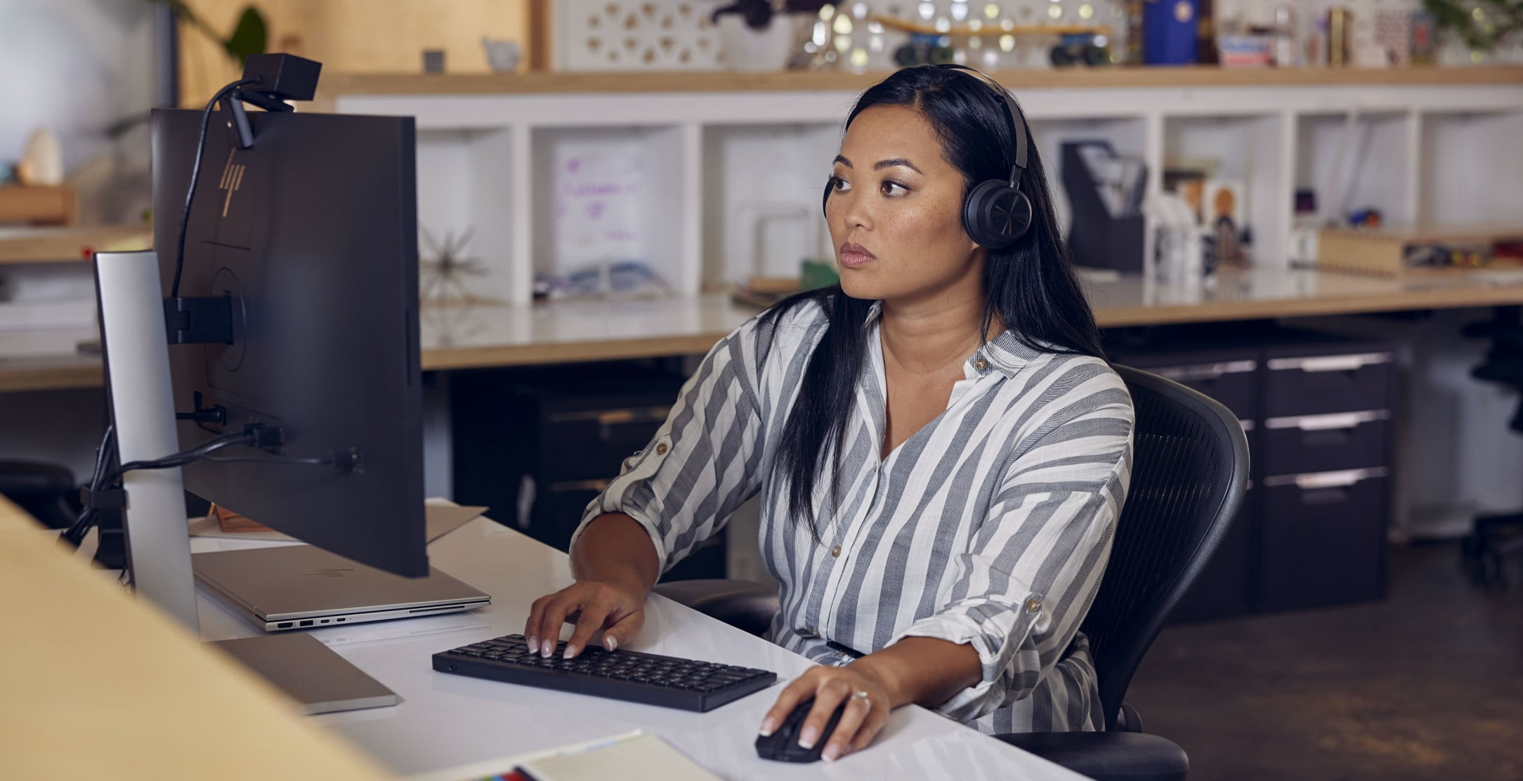 A woman working on her HP laptop connected to an HP monitor with an HP webcam and wireless keyboard and mouse.