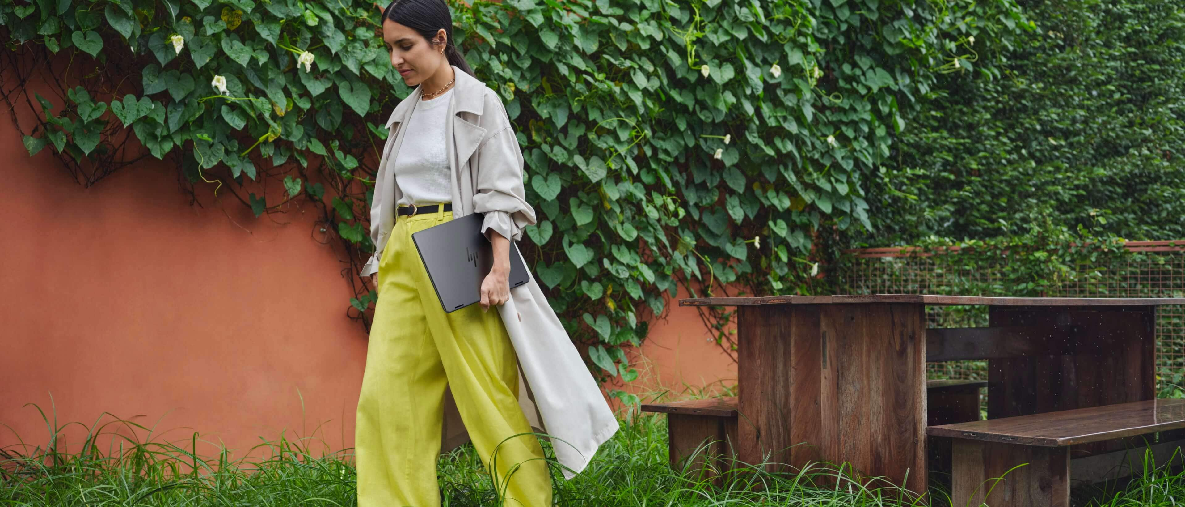 Woman wearing yellow pants walking in the street holding HP OmniBook Ultra Next Gen AI PC laptop.