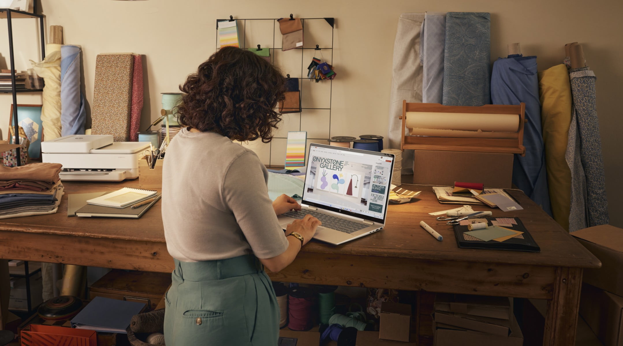 A woman checking some designs on her HP Envy laptop in top of her desk in her workshop.