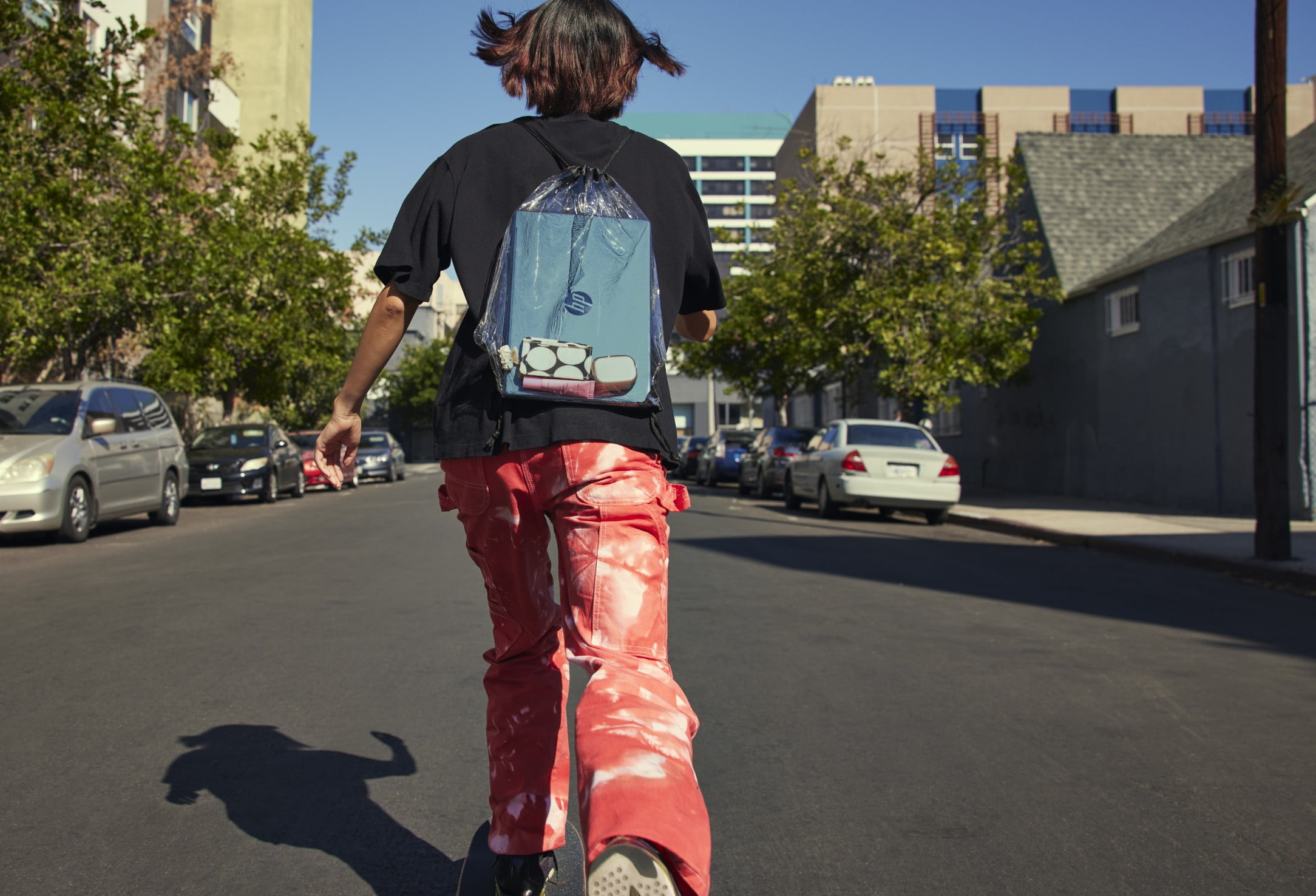 A kid skating to the school with an HP laptop inside his transparent bag on his back.