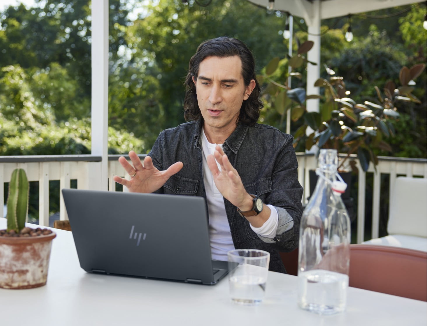 Un hombre en una conferencia virtual en una laptop HP, sentado en un jardín.