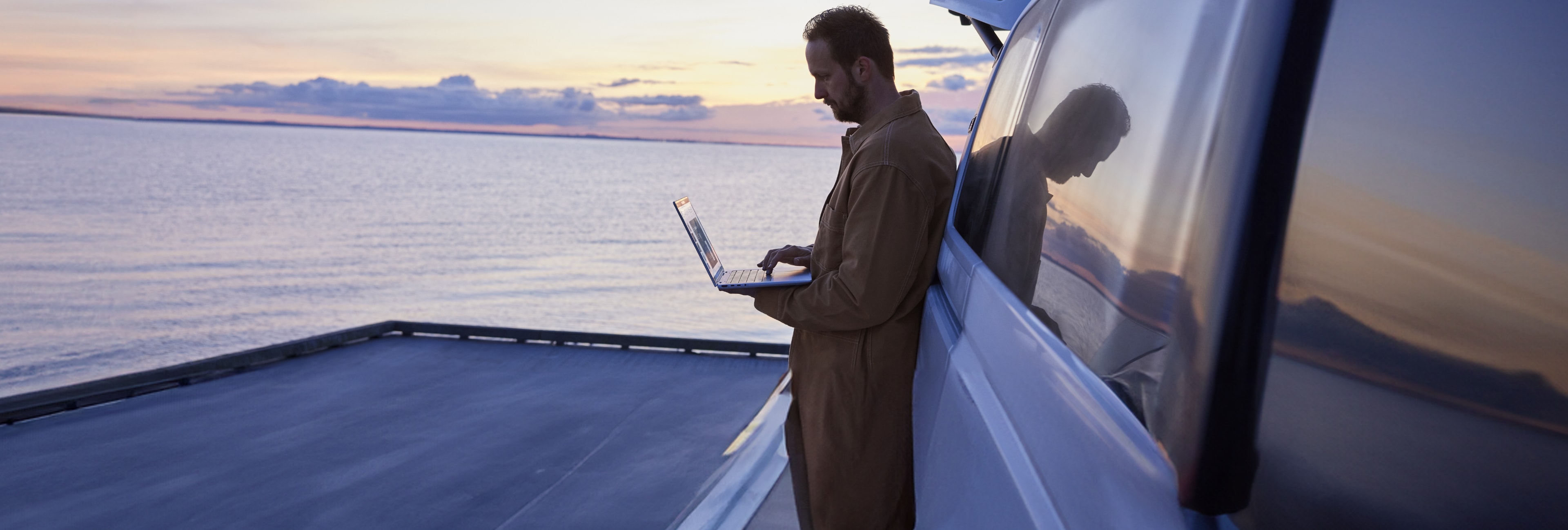 Man next to lake, working on an HP laptop outside vehicle