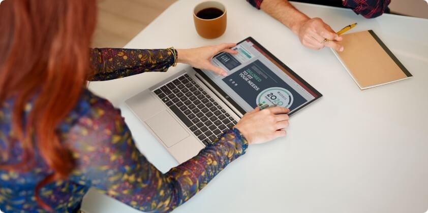 A woman showing some data to her co-worker on her HP laptop in flat mode on the desk.