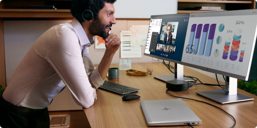 A man looking at some data on his two HP monitors connected to an HP dock and an HP laptop in closed mode.