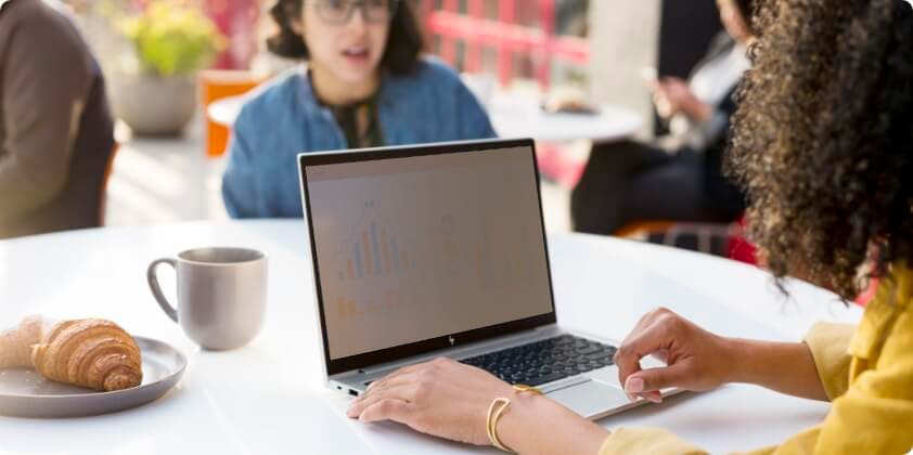 A woman looking at a presentation on her HP laptop while having a cup of coffee in a cafeteria.