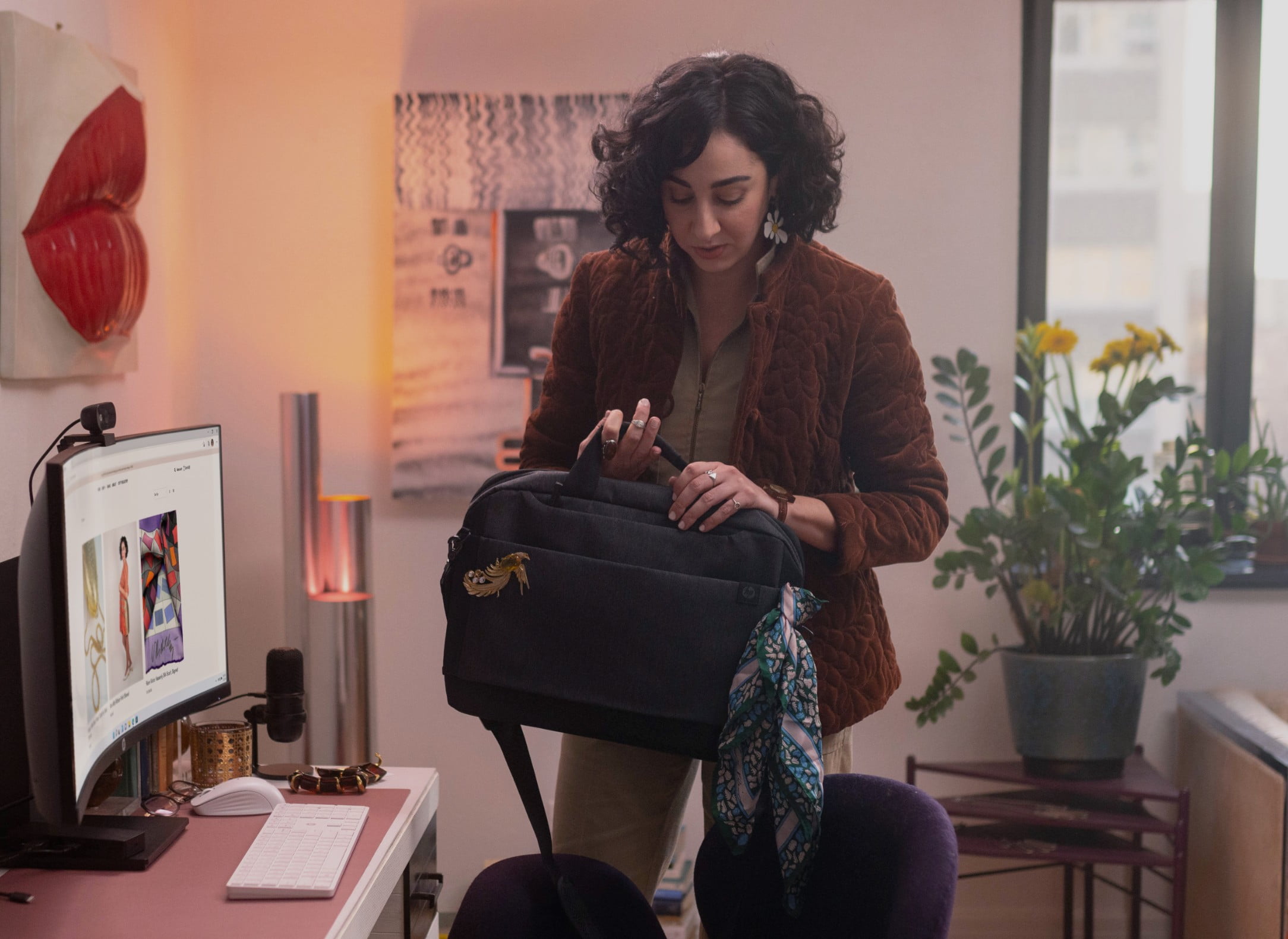 A woman picking up an HP bag while standing aside of an HP All-in-One pc on top of her desk.