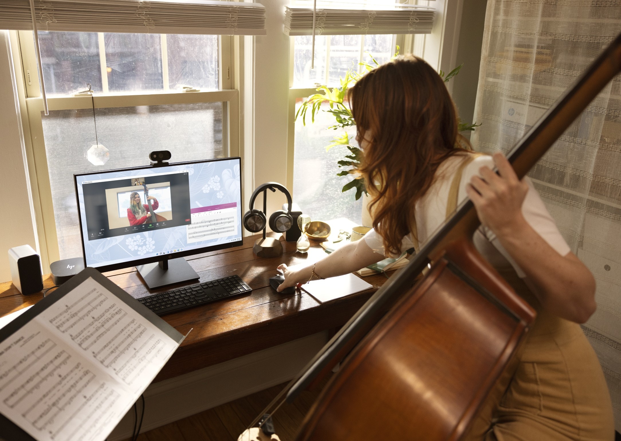 A woman looking at a video on her HP laptop connected to an HP monitor while holding a cello.