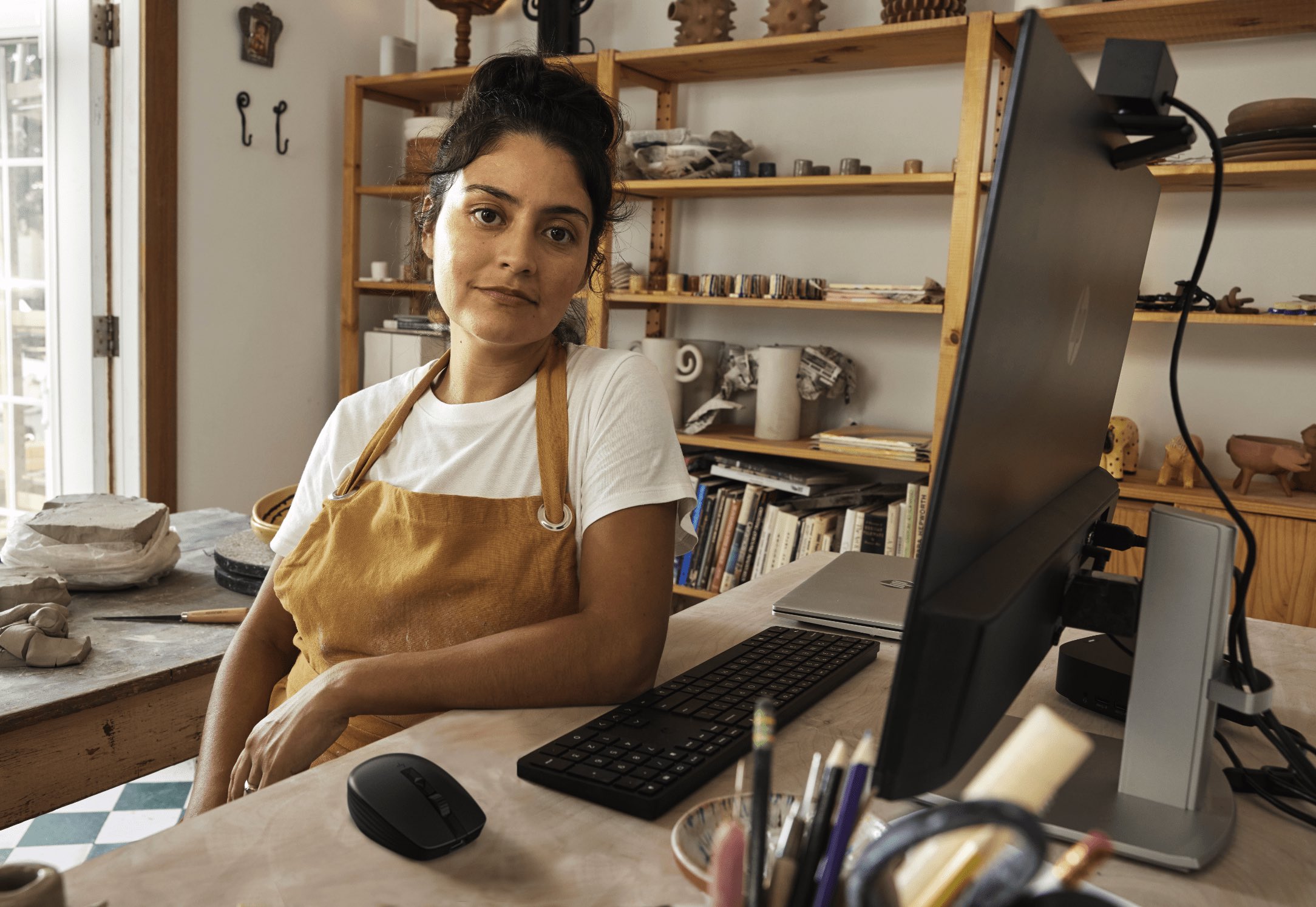 A woman sitting aside her HP monitor connected to an HP laptop with a wireless keyboard and mouse..