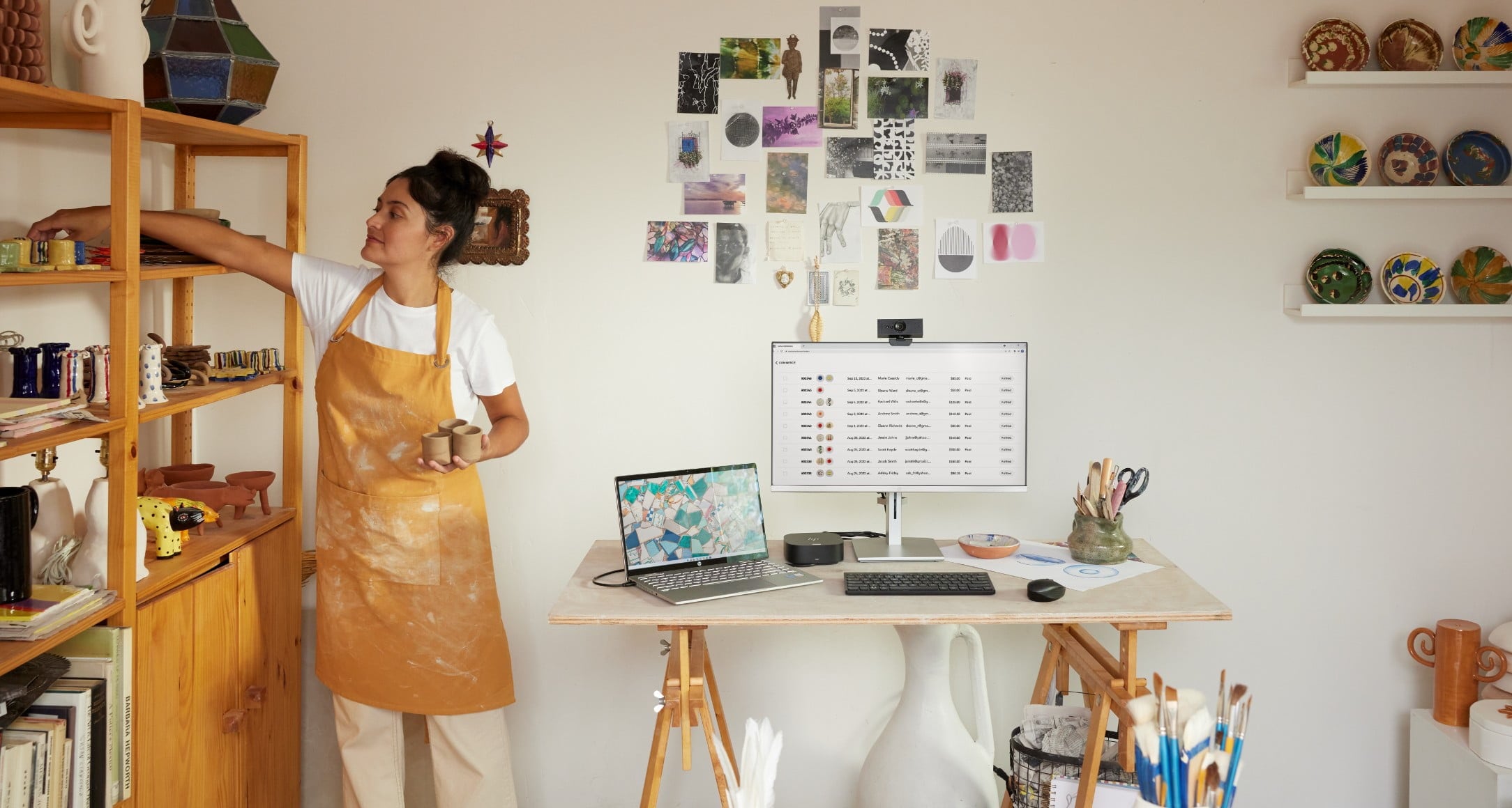 Femme en train de ranger sa poterie à côté de son ordinateur portable HP connecté à un moniteur HP avec webcam, clavier et souris sans fil HP.